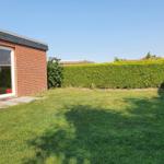 Roter Backsteinbau mit grünem Rasen und Hecke im Hintergrund.