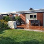 Terrasse mit Sitzgruppe, Garten und Grillplatz. Modernes Haus mit rotem Backsteinmauerwerk.