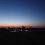 Abendlicher Hafen mit Schiffen und Kränen unter farbigem Himmel.