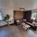 Wohnzimmer mit Ecksofa, Holzboden und großen Fenstern.