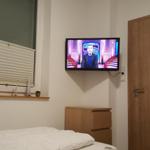 Schlafzimmer mit Bett, TV und Fenster mit Jalousie.