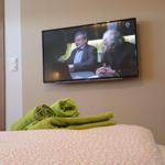 Schlafzimmer mit Bett, grünen Handtüchern und Wandfernseher.