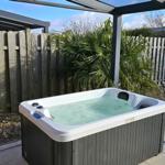 Hochwertige Whirlpool-Badewanne im Garten unter Pavillon mit Liege und Pflanzen.