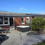 Terrasse mit Hot Tub, Loungebereich und Grillplatz. Holzzaun und Palme im Hintergrund.