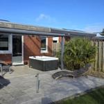 Terrasse mit Whirlpool, Sonnenliegen und Grillplatz. Hinterhof mit Holzzaun und Palme.