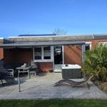 Terrasse mit Hot Tub, Sitzgruppe und Grillplatz. Garten mit Palme und Holzzaun.