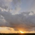 Sonnenuntergang hinter Wolken mit Straßenlaternen und Grünfläche im Vordergrund.