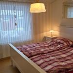 Schlafzimmer mit Bett, Nachttisch und Fenster mit Vorhängen.