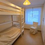 Kinderzimmer mit Doppelstockbett, Stuhl und Fenster mit Vorhängen.