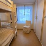 Zimmer mit Doppelstockbett, Stuhl und Kleiderschrank. Fenster mit Vorhängen.