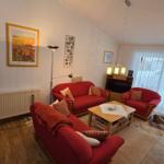 Wohnzimmer mit roten Sofas, Holztisch und großen Fenstern.
