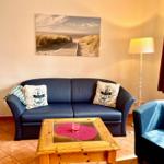 Ein Wohnzimmer mit Sofa, Sessel und Tisch. Wandbild zeigt Strand.
