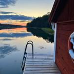 Roter Holzhaus mit Rettungsring an der Wand und Bootssteg zum See.