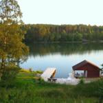 Rotes Bootshaus am See mit Holzterrasse und Liegestühlen.