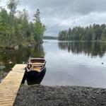 Holzboot liegt am Steg eines Sees mit Uferbereich aus Kies.