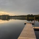 Holzsteg führt zum See. Wald im Hintergrund. Sonnenuntergang reflektiert sich im Wasser.