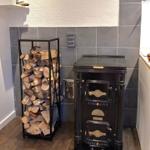 Schwarzer Ofen neben einem Holzstapel in einer Küche mit grauen Fliesen.