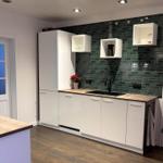 Küche mit weißen Schränken, grüner Fliesenspiegelwand und Holz Arbeitsplatte.