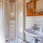 Bad mit Dusche, Waschbecken und Holzschrank an der Wand.