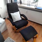 Schwarzer Sessel mit Kissen und Fußstütze vor Fenster mit Dekoration.