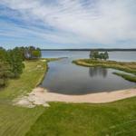 Landschaft mit See, Insel und grünem Uferbereich unter blauem Himmel.