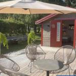 Terrasse mit Tisch und Stühlen unter einem Sonnenschirm. Hintergrund: Holzhaus mit roter Tür.