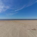 Weiterer Blick auf den Strand mit Meer und blauem Himmel.