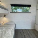Zimmer mit Doppelbett, oberem Bett und Fenster mit Blick auf Bäume.