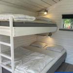 Zwei Etagenbetten mit Matratzen und Bettwäsche. Holzwand und Fenster sichtbar.