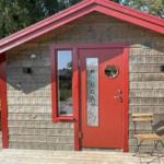 Rotes Holzhaus mit Tür und Fenster, zwei Stühle draußen.