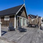 Holzterrasse mit Liegestühlen und Tisch. Hintergrund: Holzhaus mit Fenstern und Dach.