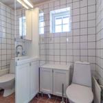 Badezimmer mit Toilette, Waschbecken und Spiegelschrank. Weiße Fliesen und kleines Fenster.
