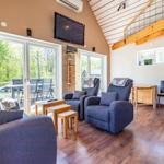 Wohnzimmer mit Sofa, zwei Sesseln und Holzboden. Große Fenster, TV und Treppe.