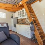 Küche mit Arbeitsplatte, Schränken und Fenster. Holztreppe führt nach oben. Sitzgelegenheit mit Kissen.