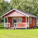 Rotes Holzhaus mit weißem Vordach und Blumenkasten auf grünem Rasen.