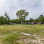 Grünes Feld mit Fußballtor und mehreren Holzhütten im Hintergrund.