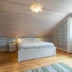 Schlafzimmer mit Holzdecke, floraler Tapete und weißem Bett.