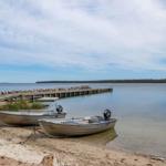 Zwei Motorboote liegen am Strand vor einem Steg.
