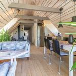Wohn- und Essbereich mit Holzdecke, Sofa, Tisch und Küchenspüle.