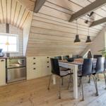 Küche mit Essbereich unter Holzdach, Küchenschränke, Tisch mit Stühlen und Pflanze.