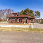 Ein Haus mit rotem Dach und Fensterrahmen steht auf einem Grundstück mit Gras und Bäumen.