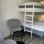 Zimmer mit Schlafcouch und Doppelbett, graue Sitzgelegenheit und kleiner Tisch.