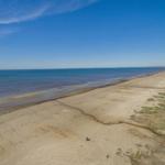 Weiterer Strandabschnitt mit sandigem Ufer und ruhigem Meer unter blauem Himmel.