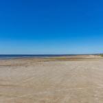 Weiterer Sandstrand mit klarem Himmel und ruhigem Meer im Hintergrund.