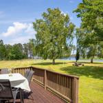 Terrasse mit Tisch und Stühlen, Blick auf Grasfläche und See.