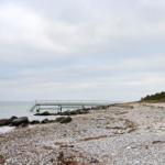 Steiniger Strand mit Bootssteg und Blick aufs Meer.