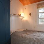 Schlafzimmer mit Bett, Kleiderschrank und Fenster. Wände mit weißen Paneelen, Holzdecke.