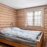 Schlafzimmer mit Holzwand, Bett und Fenster mit Vorhang.
