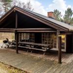 Holzhaus mit überdachtem Balkon, Picknicktisch und Grill. Umgeben von Wald.