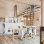 Dining area with table and chairs, wood-burning stove, and kitchen with wooden walls.